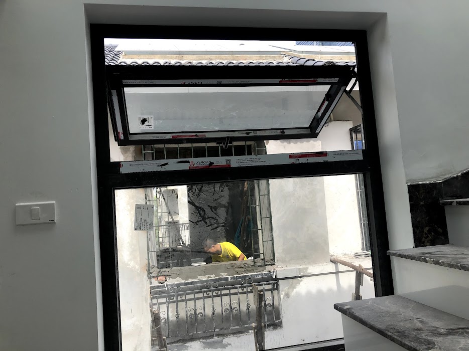 Cửa sổ nhôm kính khung đen đang lắp đặt tại nhà phố, phía ngoài có thợ xây dựng làm việc